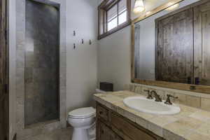 Bathroom featuring vanity, a tile shower, and toilet