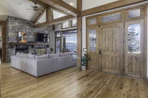 Entryway featuring light hardwood / wood-style floors, ceiling fan, a fireplace, high vaulted ceiling, and beam ceiling