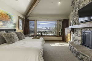 Carpeted bedroom with a stone fireplace and vaulted ceiling with beams