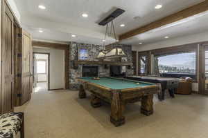 Game room with pool table, beamed ceiling, a stone fireplace, and light carpet