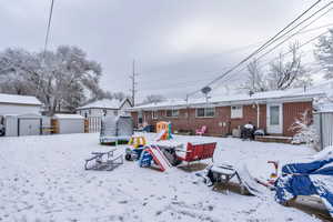 Snow covered house featuring a trampoline, a storage shed, and a playground