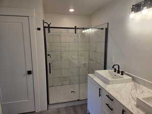 Full bathroom featuring a shower stall, double vanity, and wood finished floors