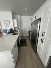 Kitchen featuring light hardwood / wood-style flooring, sink, light stone counters, stainless steel appliances, and white cabinets