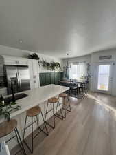 Kitchen with hanging light fixtures, a breakfast bar, stainless steel fridge, white cabinetry, and kitchen peninsula