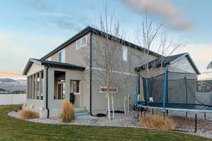 Back house at dusk with a trampoline, a lawn, and a sunroom