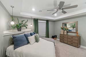 Bedroom with a raised ceiling, light carpet, and ceiling fan