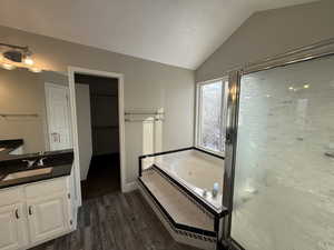 Bathroom featuring lofted ceiling, a spacious closet, vanity, wood finished floors, and a whirlpool tub