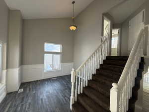 Stairs featuring wainscoting, visible vents, a high ceiling, and wood finished floors