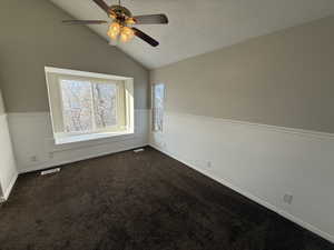 Spare room with visible vents, lofted ceiling, ceiling fan, a textured ceiling, and dark carpet