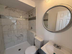 Bathroom with toilet, a tile shower, and vanity