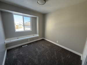 Empty room featuring a textured ceiling, dark carpet, visible vents, and baseboards