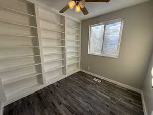 Empty room featuring built in shelves, dark wood-style flooring, visible vents, ceiling fan, and baseboards