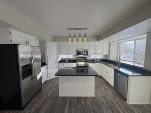 Kitchen with a kitchen island, appliances with stainless steel finishes, decorative light fixtures, white cabinetry, and a sink