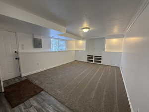 Basement with a textured ceiling, wood finished floors, electric panel, and baseboards