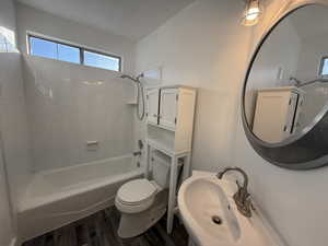 Bathroom with toilet, a sink, wood finished floors, and bathing tub / shower combination