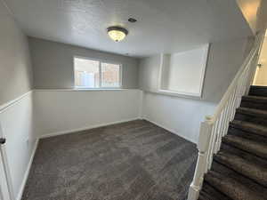 Basement featuring baseboards, dark carpet, stairway, and a textured ceiling