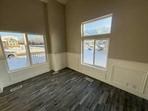 Empty room featuring a wainscoted wall, visible vents, and dark wood-type flooring