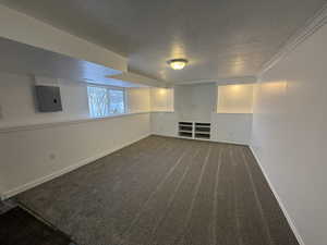 Below grade area with carpet floors, electric panel, a textured ceiling, and baseboards