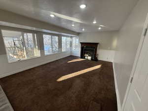 Unfurnished living room featuring recessed lighting, dark carpet, a fireplace with flush hearth, a textured ceiling, and baseboards