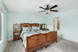 Bedroom with ensuite bathroom, ceiling fan, and light colored carpet