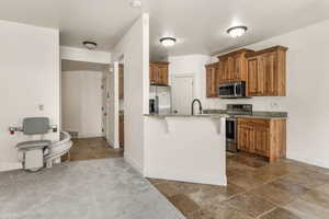 Kitchen with appliances with stainless steel finishes, sink, light stone counters, kitchen peninsula, and a breakfast bar area