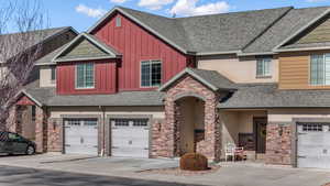 View of front of home with a shingled roof, board and batten siding, a garage, stone siding, and driveway