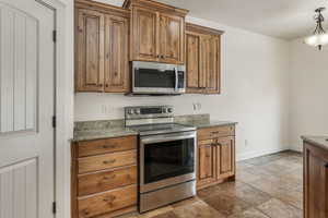 Kitchen with hanging light fixtures, appliances with stainless steel finishes, and light stone counters