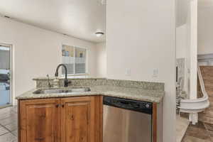 Kitchen featuring kitchen peninsula, sink, dishwasher, light stone counters, and light tile patterned floors