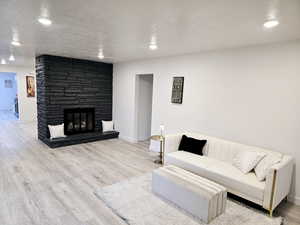 Living room with a fireplace, light wood-type flooring, and a textured ceiling