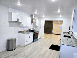 Kitchen featuring dark stone counters, wall chimney exhaust hood, stainless steel electric range, light wood-type flooring, and a sink