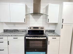 Kitchen with white cabinets, stainless steel electric stove, wall chimney range hood, and stone counters
