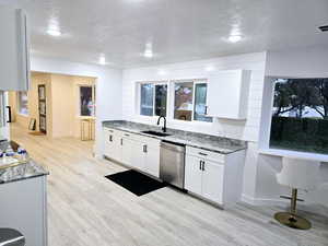 Kitchen featuring sink, white cabinetry, dishwasher, dark stone counters, and light hardwood / wood-style floors