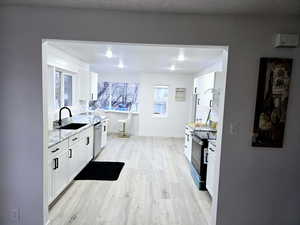 Kitchen featuring light wood finished floors, white cabinets, black electric range, stainless steel dishwasher, and a sink