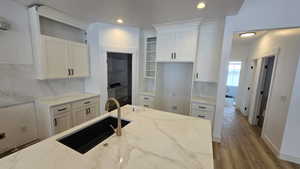 Kitchen with wood-type flooring, sink, light stone countertops, and white cabinets