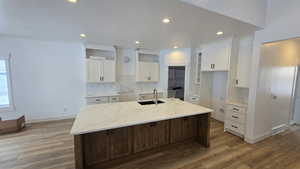 Kitchen featuring an island with sink, sink, light stone counters, wood-type flooring, and white cabinets