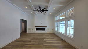 Unfurnished living room featuring coffered ceiling, beamed ceiling, a towering ceiling, ceiling fan, and dark hardwood / wood-style flooring