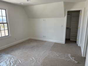 Unfurnished bedroom featuring a spacious closet, light carpet, lofted ceiling, and baseboards