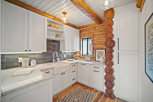 Kitchen with beamed ceiling, sink, white cabinets, backsplash, and light wood-type flooring