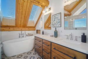 Bathroom with wooden ceiling, vanity, vaulted ceiling with skylight, and a tub