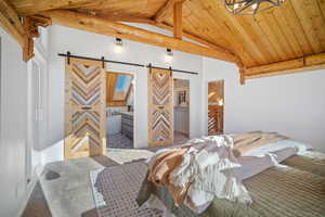 Carpeted bedroom with a barn door, vaulted ceiling with beams, and wood ceiling