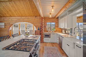 Kitchen with white cabinetry, appliances with stainless steel finishes, hanging light fixtures, and plenty of natural light