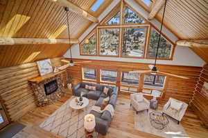 Living room with a stone fireplace, a skylight, high vaulted ceiling, wooden ceiling, and ceiling fan