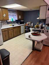 Kitchen with white appliances, light wood-type flooring, sink, and backsplash