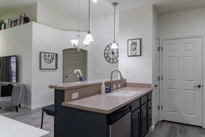 Kitchen with kitchen peninsula, decorative light fixtures, sink, stainless steel dishwasher, and dark wood-type flooring