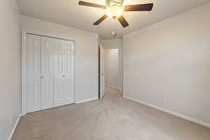 Unfurnished bedroom featuring ceiling fan, a closet, a textured ceiling, and light colored carpet