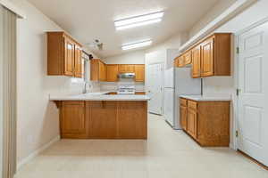 Kitchen with sink, white appliances, kitchen peninsula, and lofted ceiling