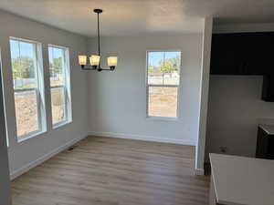 Unfurnished dining area with a healthy amount of sunlight, light hardwood / wood-style flooring, a textured ceiling, and a notable chandelier