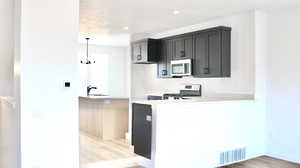 Kitchen with light wood-type flooring, stainless steel appliances, decorative light fixtures, sink, and kitchen peninsula