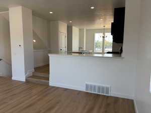 Kitchen featuring kitchen peninsula, decorative light fixtures, sink, wood-type flooring, and a chandelier