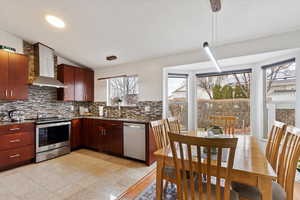 Kitchen featuring tasteful backsplash, stainless steel appliances, wall chimney range hood, pendant lighting, and sink